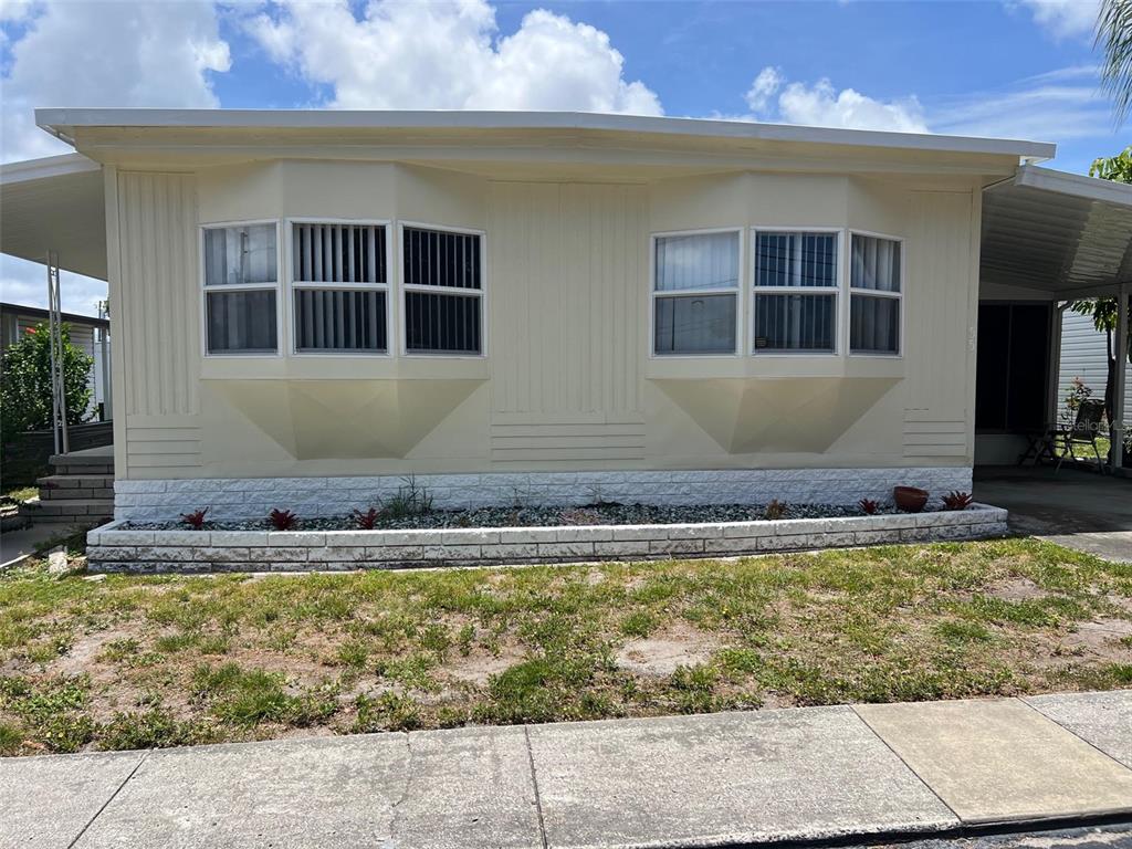 The exterior of a light-colored mobile home features two bay windows and a stone-textured base — 12651 SEMINOLE BOULEVARD UNIT 55, LARGO, FL