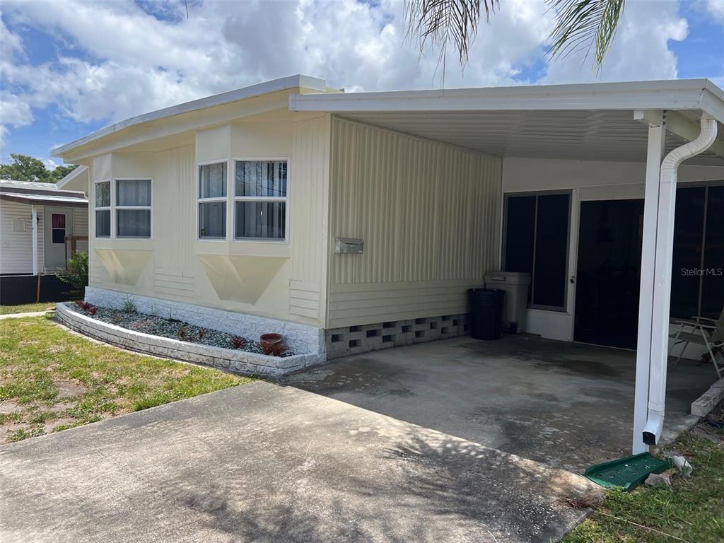 A light-colored mobile home features a concrete driveway, a carport, and a stone-bordered garden bed — 12651 SEMINOLE BOULEVARD UNIT 55, LARGO, FL