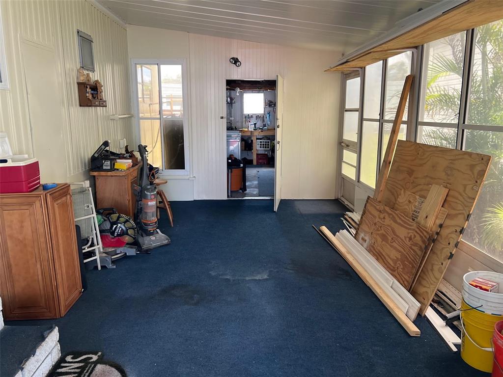 A sunroom with blue carpeting, white paneled walls, and a doorway leading to a workshop — 12651 SEMINOLE BOULEVARD UNIT 55, LARGO, FL