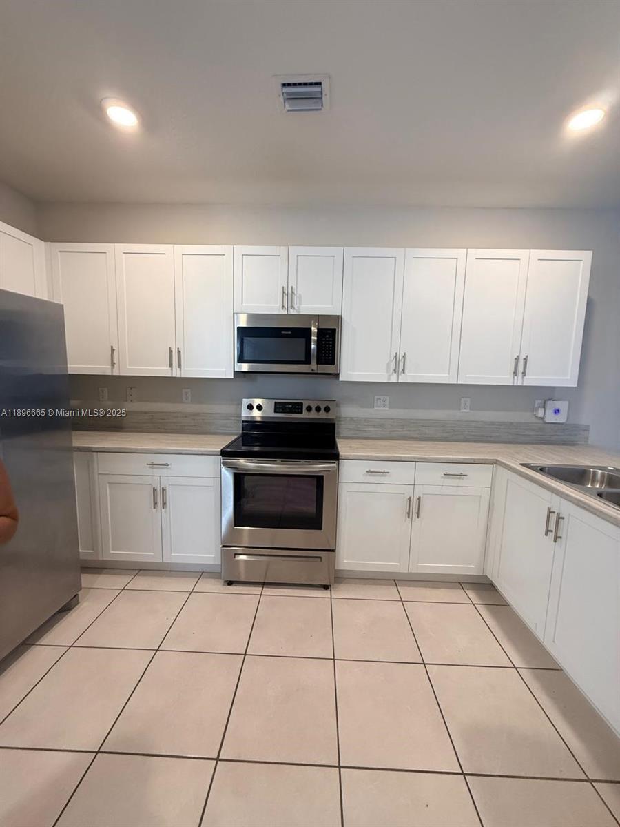 A kitchen features white cabinets, stainless steel appliances, and light-colored tile flooring — 12715 SW 230th Ter, Miami FL 33170, MIAMI, FL
