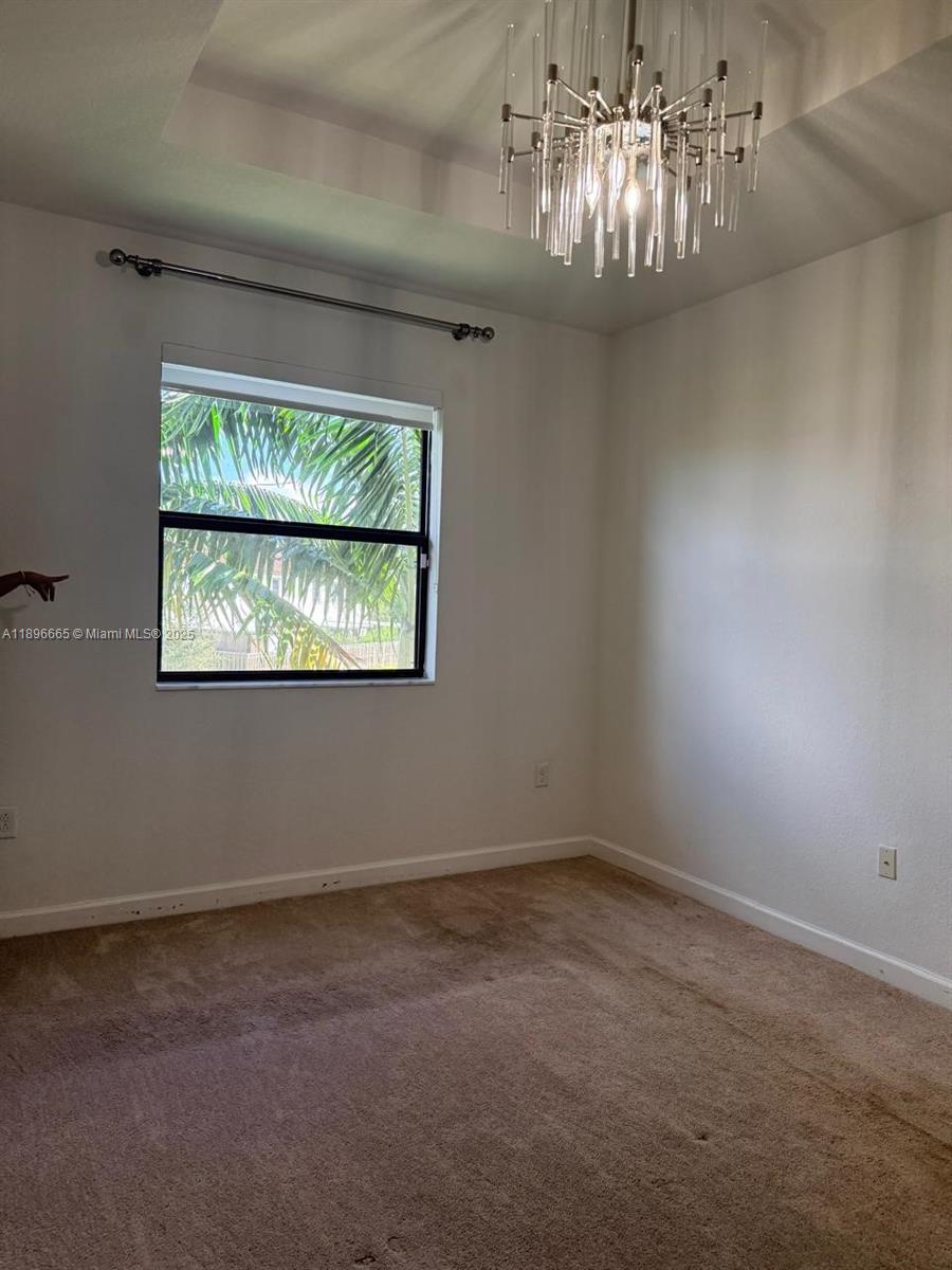 A bedroom features beige carpeting, a tray ceiling, and a modern glass-rod chandelier — 12715 SW 230th Ter, Miami FL 33170, MIAMI, FL