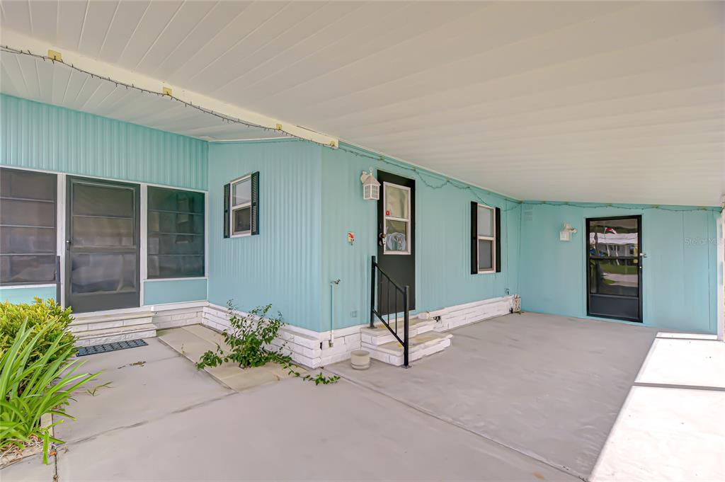 A light blue mobile home exterior features a covered concrete carport and two entry doors — 3922 WILLIAM HUME DRIVE, ZEPHYRHILLS, FL
