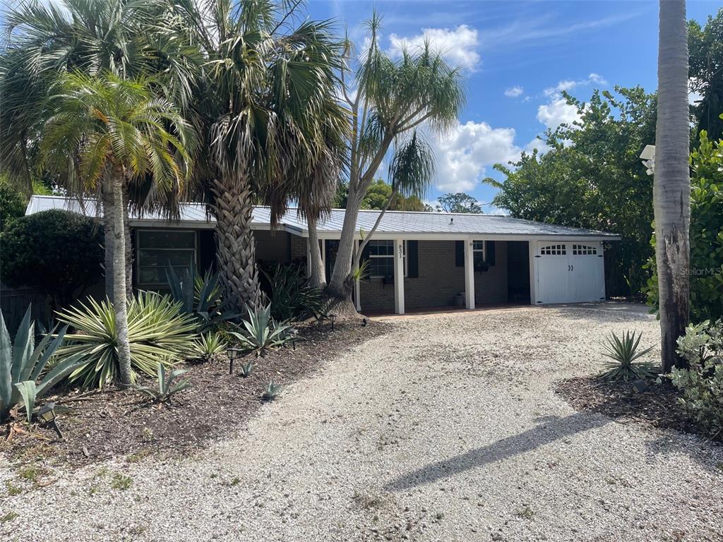 A single-story house with a gravel driveway, metal roof, and palm trees in front — 831 40TH STREET, SARASOTA, FL