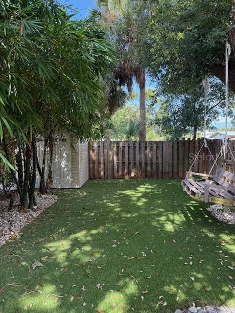 A backyard features artificial turf, a wooden fence, a storage shed, and a hanging swing — 831 40TH STREET, SARASOTA, FL