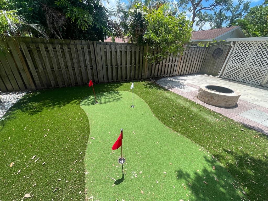 A backyard putting green with three holes and flags sits next to a stone fire pit — 831 40TH STREET, SARASOTA, FL