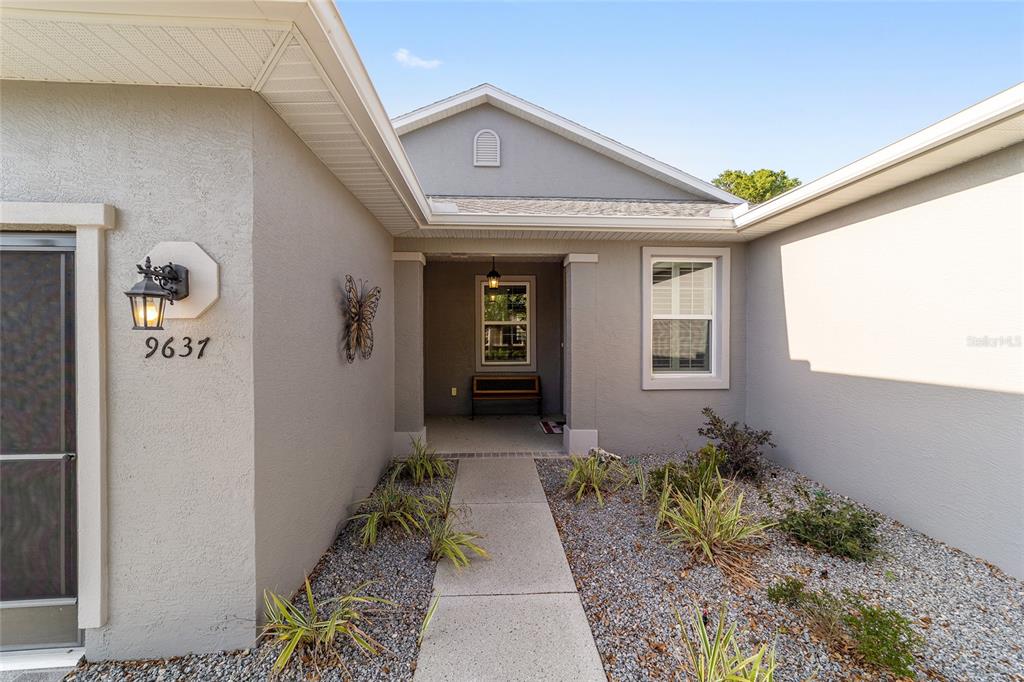 A concrete walkway leads to the covered entryway of a gray stucco house — 9637 SW 95TH LOOP, OCALA, FL
