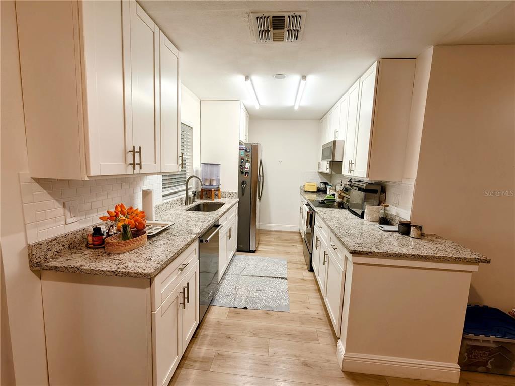 A galley kitchen features white cabinets, granite countertops, stainless steel appliances, and wood-look flooring — 49 W MARBRISA WAY, KISSIMMEE, FL
