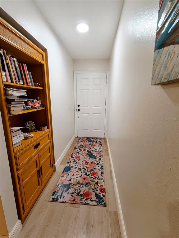A hallway features a wooden bookshelf, a floral runner rug, and a white front door — 49 W MARBRISA WAY, KISSIMMEE, FL