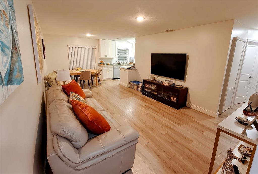 A living room with light wood-look flooring, a beige sofa, and an open kitchen area — 49 W MARBRISA WAY, KISSIMMEE, FL