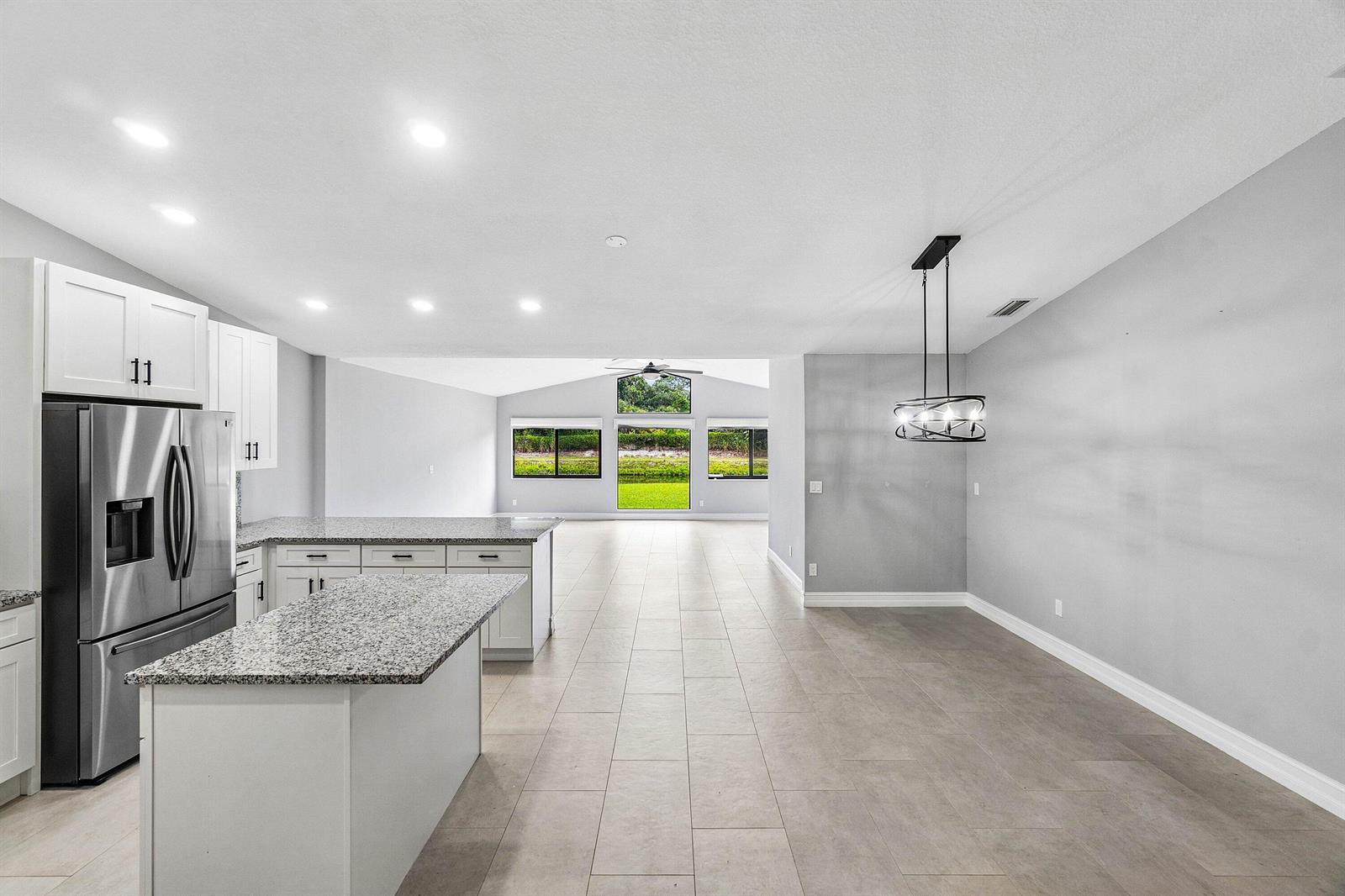 A kitchen with granite countertops and stainless steel appliances opens to a dining area — 120 Mayfair Lane, Boynton Beach FL 33426, BOYNTON BEACH, FL
