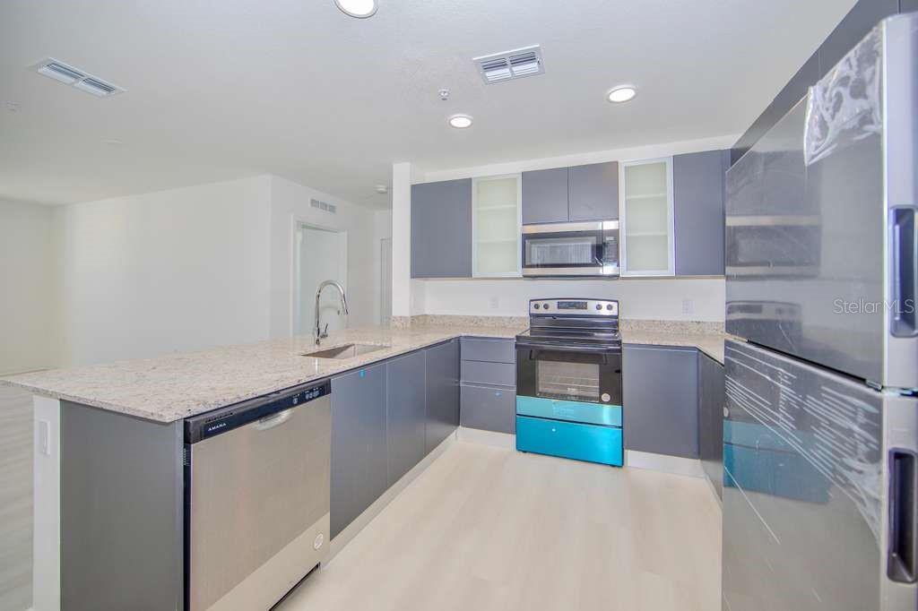 A modern kitchen features gray cabinets, granite countertops, stainless steel appliances, and light-colored flooring — 5579 MILLENIA PARK BLVD UNIT 511, ORLANDO, FL