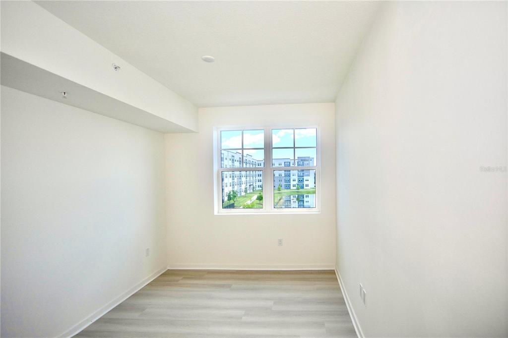 An empty room with light-colored wood-look flooring, white walls, and a window overlooking buildings — 5579 MILLENIA PARK BLVD UNIT 511, ORLANDO, FL