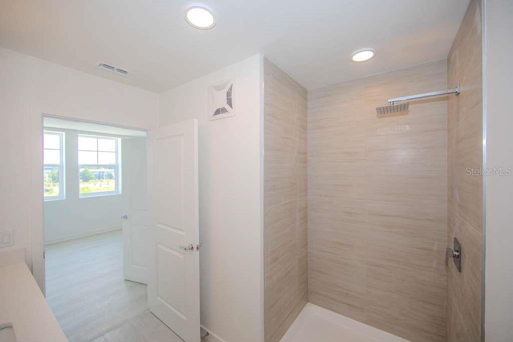 A modern bathroom features a walk-in shower with light-colored tile and a rainfall showerhead — 5579 MILLENIA PARK BLVD UNIT 511, ORLANDO, FL