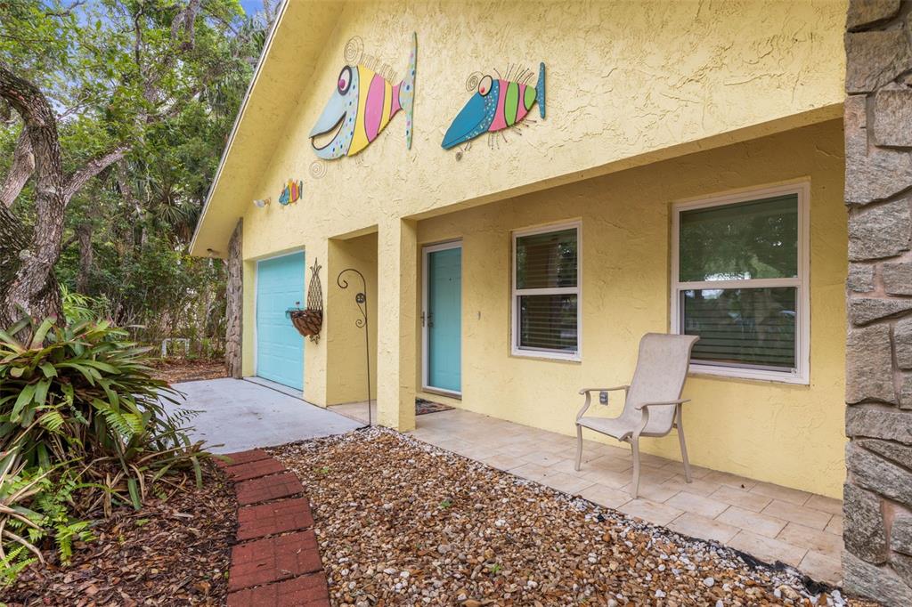 A yellow house exterior features two decorative fish wall hangings, a blue door, and patio — 1436 S FLAGLER AVENUE, FLAGLER BEACH, FL