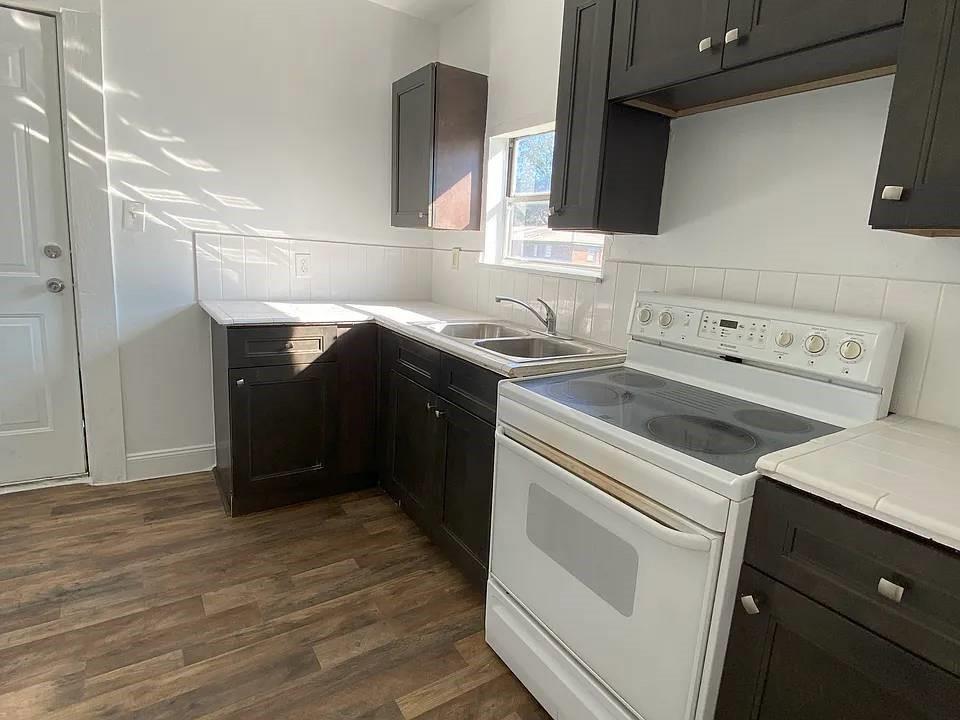 A kitchen features dark wood cabinets, white tile countertops, a white electric stove, and wood-look flooring — 4144 Herring Avenue, FL 32448, FL