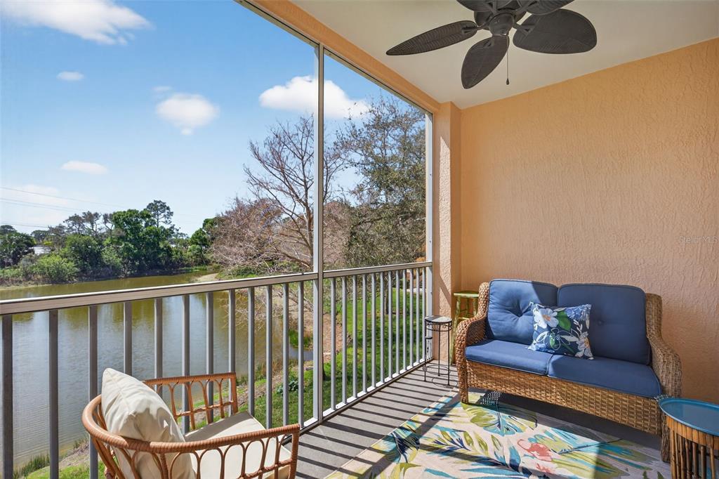 A screened-in balcony with wicker furniture overlooks a pond and trees under a blue sky — 4138 CENTRAL SARASOTA PARKWAY UNIT 1526, SARASOTA, FL