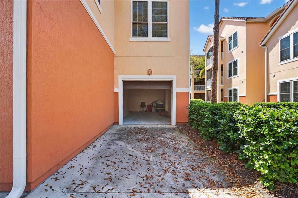 An open garage with a concrete driveway and scattered leaves in front of a building — 4138 CENTRAL SARASOTA PARKWAY UNIT 1526, SARASOTA, FL