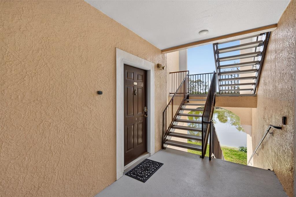 An exterior view of an apartment entryway with a brown door and metal stairs — 4138 CENTRAL SARASOTA PARKWAY UNIT 1526, SARASOTA, FL