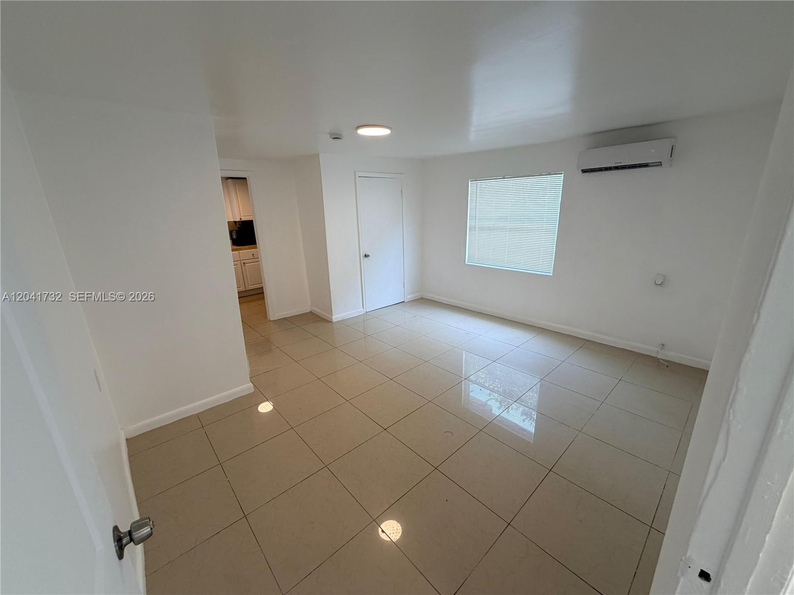An empty room features white walls, light-colored tile flooring, a window with blinds, and an AC unit — 548 NW 30th St # 2, Miami FL 33127, MIAMI, FL