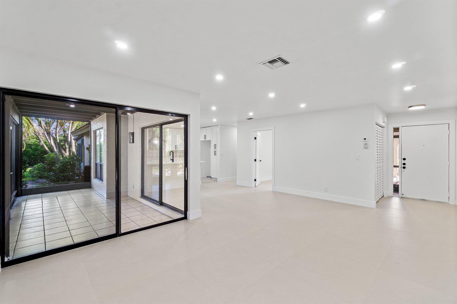 A bright, open-concept living area features white tile floors, recessed lighting, and sliding glass doors — 5944 Forest Grove Drive # 3, Boynton Beach FL 33437, BOYNTON BEACH, FL