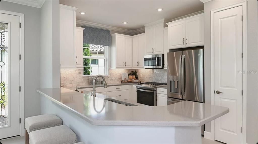 A kitchen features white cabinets, stainless steel appliances, a quartz countertop, and a breakfast bar — 3213 TORTA COURT, BRADENTON, FL
