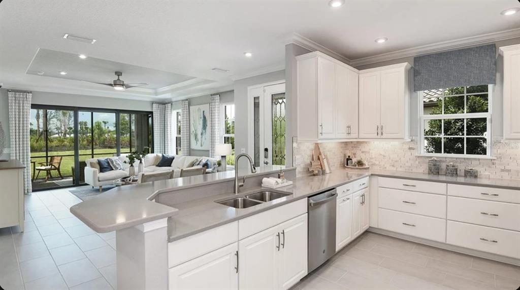 A kitchen with white cabinets and gray countertops overlooks a living room with sliding doors — 3213 TORTA COURT, BRADENTON, FL
