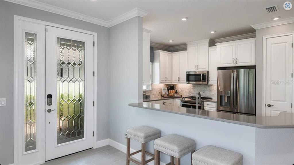 A kitchen with white cabinets and a breakfast bar sits next to a front door — 3213 TORTA COURT, BRADENTON, FL