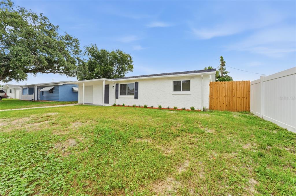 A white single-story house with a flat roof, dark shutters, and a wooden side fence — 3306 CANTRELL STREET, HOLIDAY, FL
