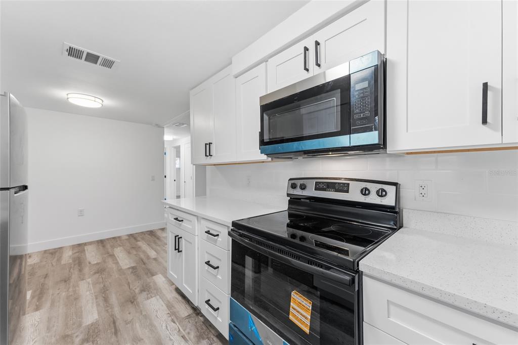A kitchen features white cabinets, stainless steel appliances, and light wood-look flooring — 3306 CANTRELL STREET, HOLIDAY, FL