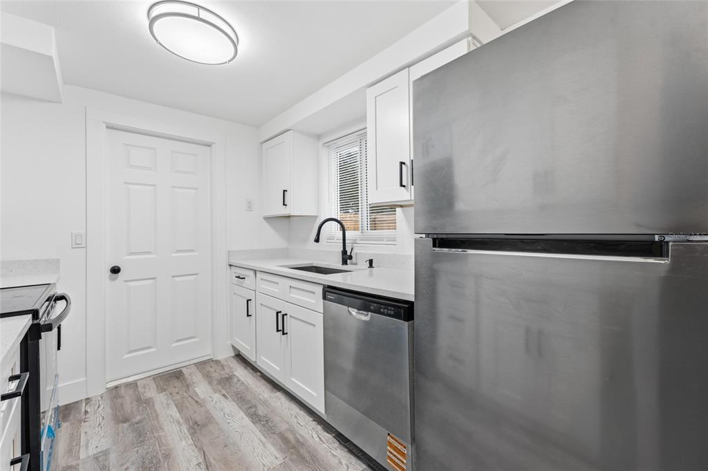A kitchen features white cabinets, stainless steel appliances, a dark faucet, and wood-look flooring — 3306 CANTRELL STREET, HOLIDAY, FL