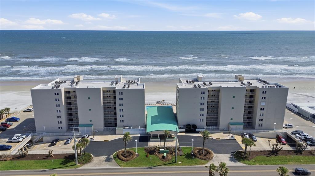 An aerial view shows two multi-story apartment buildings situated directly on a sandy beach — 4495 S ATLANTIC AVENUE UNIT 501, PORT ORANGE, FL