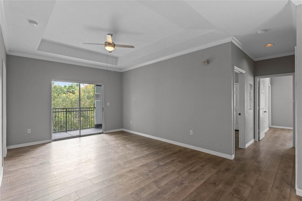 A living room with gray walls, wood-look flooring, a tray ceiling, and a sliding glass door — 5501 PGA BOULEVARD UNIT 4724, ORLANDO, FL