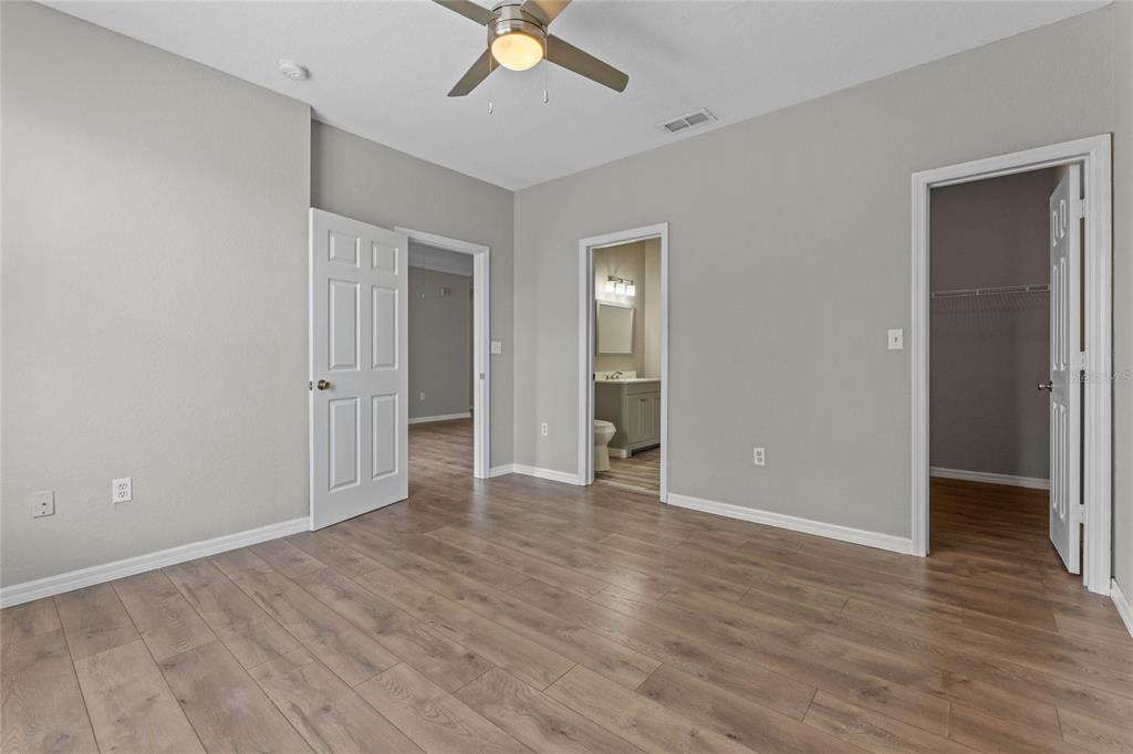 An empty bedroom with light gray walls, wood-look flooring, a ceiling fan, and three doorways — 5501 PGA BOULEVARD UNIT 4724, ORLANDO, FL