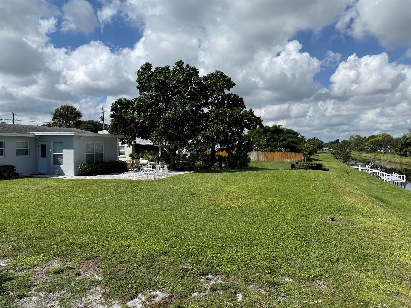 A backyard with a patio, large tree, and lawn leading to a canal with docks — 2623 Northside Drive, Lake Worth FL 33462, LAKE WORTH, FL
