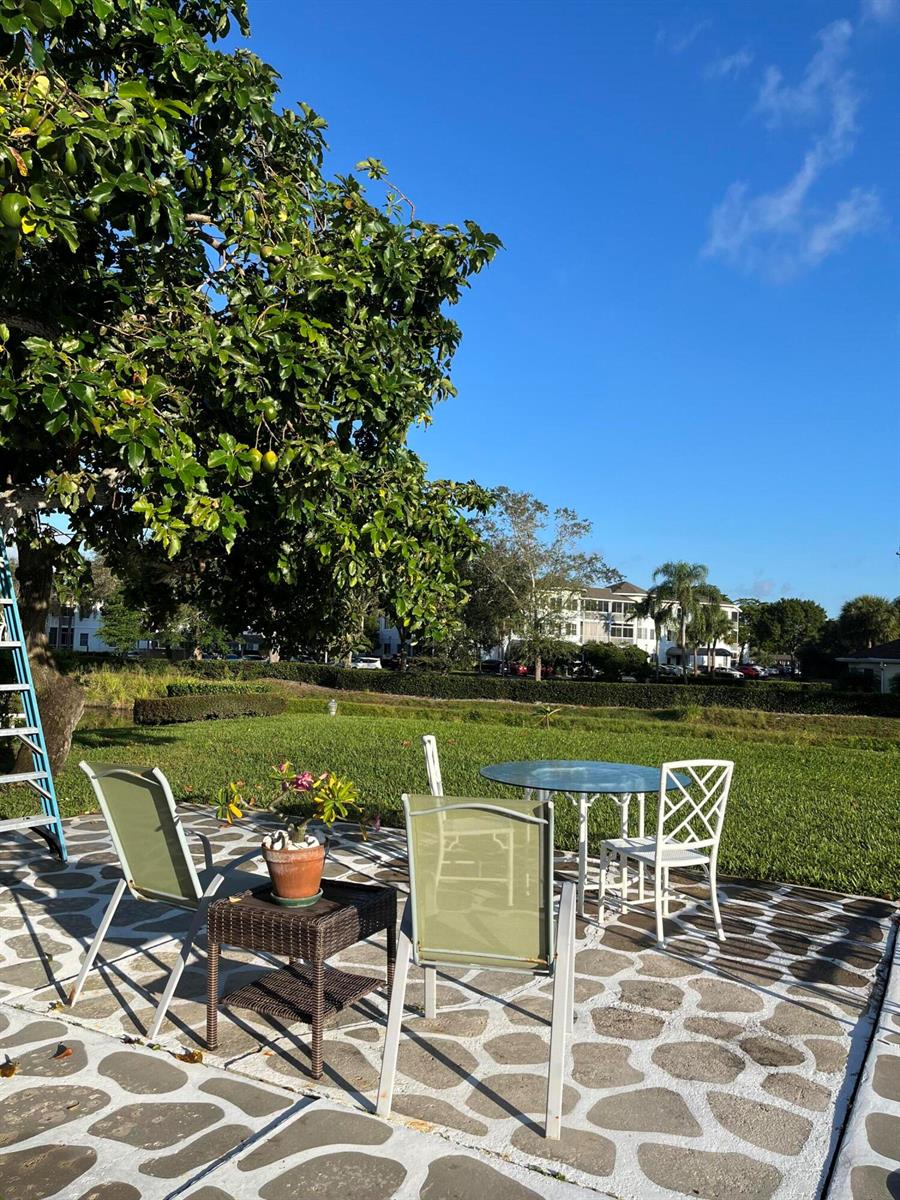A stone patio features a glass table, chairs, and a potted plant under a tree — 2623 Northside Drive, Lake Worth FL 33462, LAKE WORTH, FL