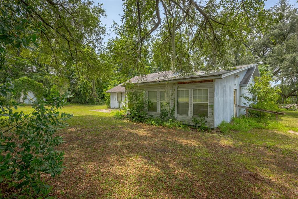 A weathered, single-story house with light-colored siding sits on a grassy lot under large trees — 276 SW TABERNACLE GLEN, LAKE CITY, FL