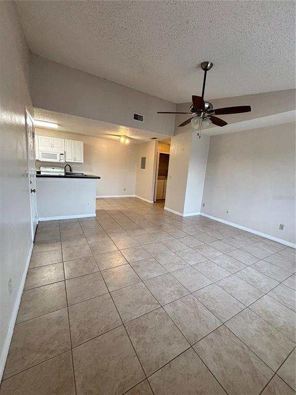 An open-concept living area features light-colored tile flooring, a ceiling fan, and a kitchen — 2030 CASCADES BOULEVARD UNIT 303, KISSIMMEE, FL