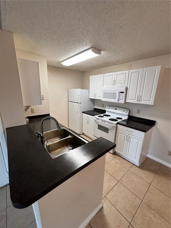 A kitchen features white cabinets, black countertops, a double-basin sink, and white appliances — 2030 CASCADES BOULEVARD UNIT 303, KISSIMMEE, FL