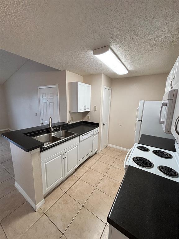 A kitchen features white cabinets, black countertops, tile flooring, and a white appliance suite — 2030 CASCADES BOULEVARD UNIT 303, KISSIMMEE, FL