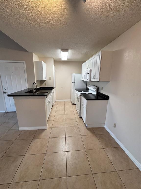 A kitchen features white cabinets, black countertops, tile flooring, and white appliances — 2030 CASCADES BOULEVARD UNIT 303, KISSIMMEE, FL