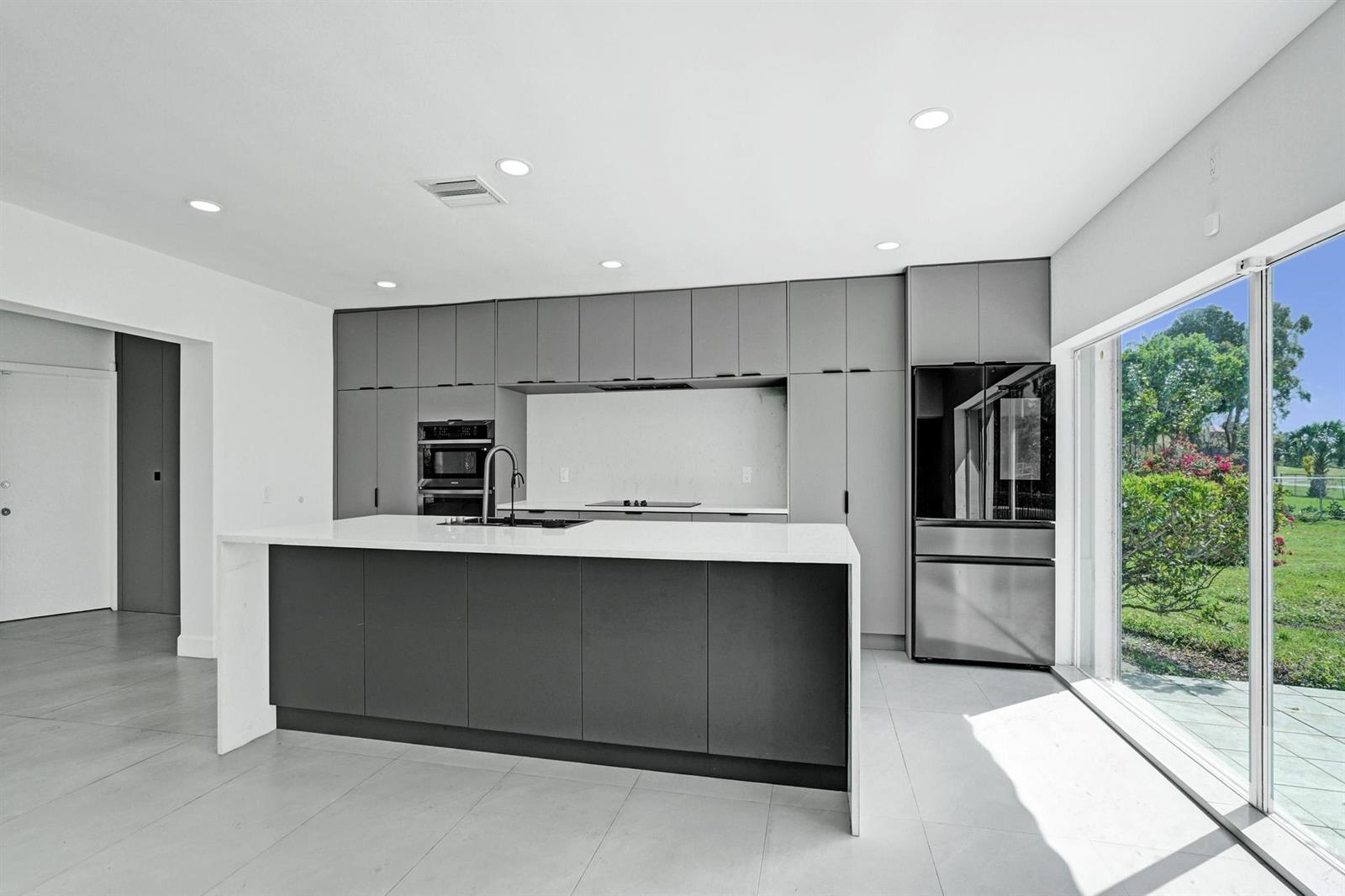 A modern kitchen features gray cabinetry, a white island, and a sliding glass door — 6700 E Tropical Way, Plantation FL 33317, PLANTATION, FL