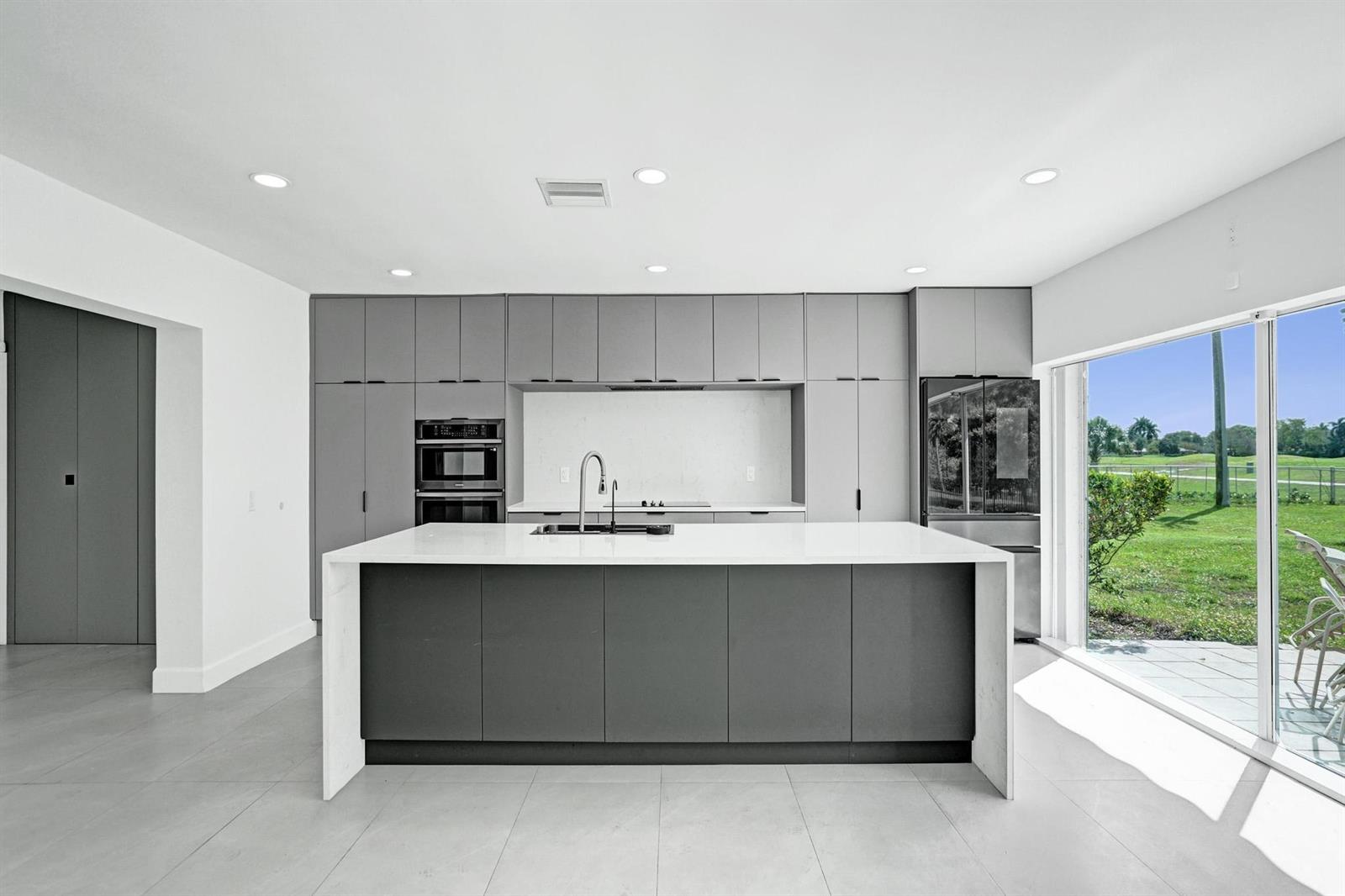 A modern kitchen features gray cabinetry, a white waterfall island, and a large sliding glass door — 6700 E Tropical Way, Plantation FL 33317, PLANTATION, FL
