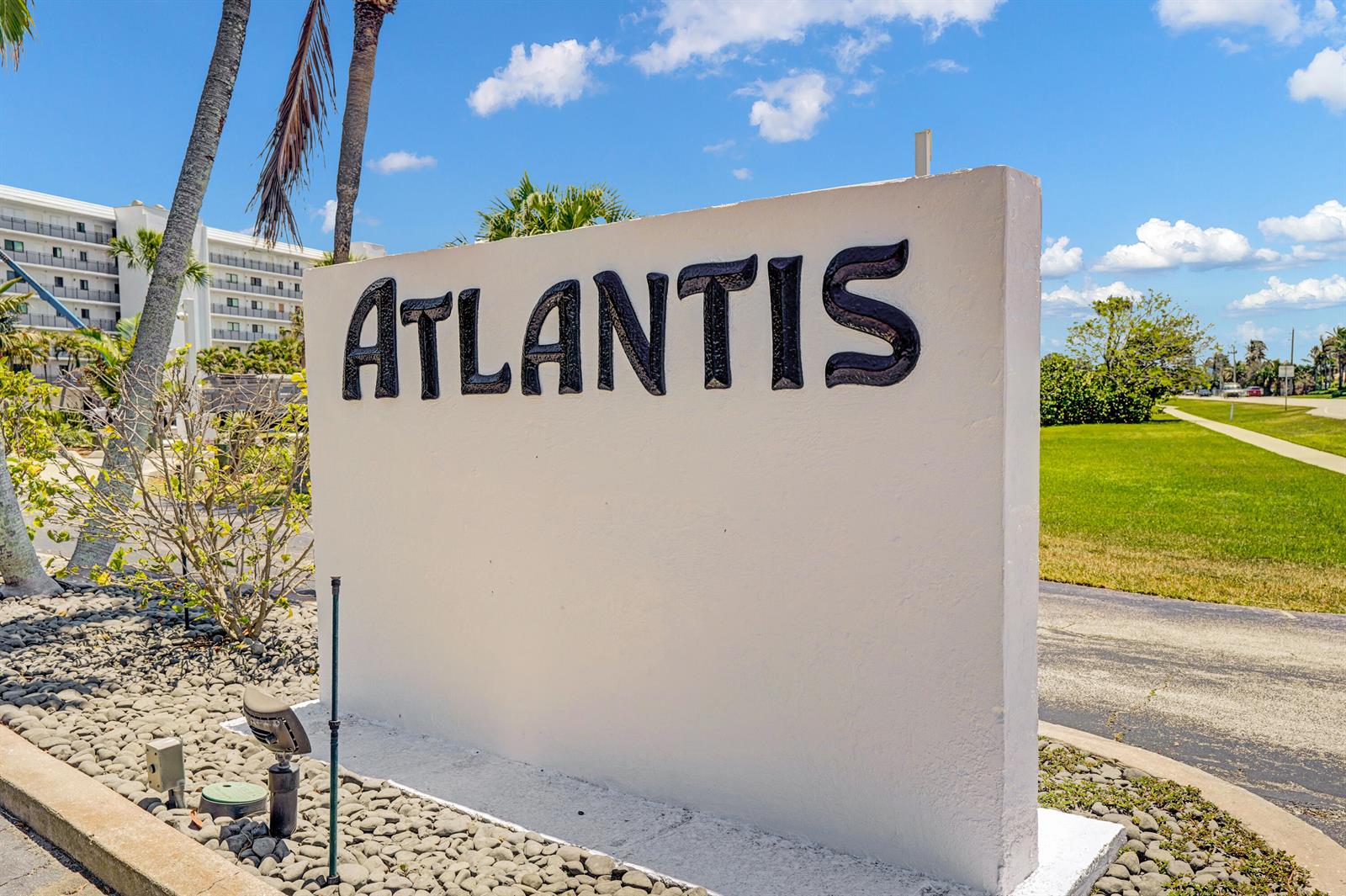 A white sign with the word Atlantis in black letters stands outdoors near palm trees — 10200 S Ocean Drive # 104, Jensen Beach FL 34957, JENSEN BEACH, FL