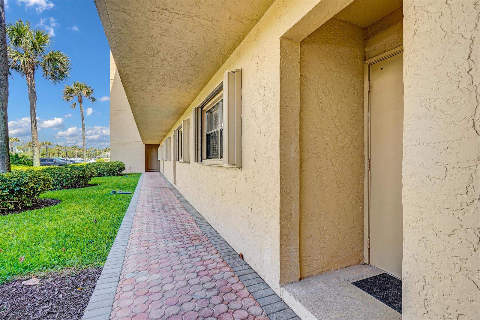 A paved walkway runs along the exterior of a tan building with windows and doors — 10200 S Ocean Drive # 104, Jensen Beach FL 34957, JENSEN BEACH, FL