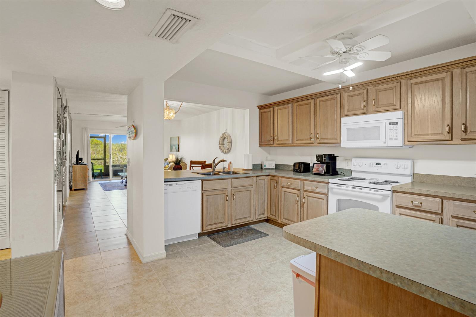 A kitchen with wood cabinets, white appliances, and a peninsula overlooks a living area — 10200 S Ocean Drive # 104, Jensen Beach FL 34957, JENSEN BEACH, FL