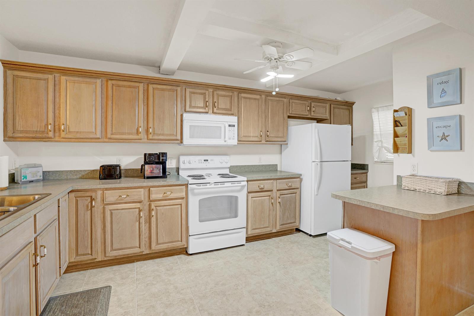 A kitchen features light wood cabinets, white appliances, and a white ceiling fan — 10200 S Ocean Drive # 104, Jensen Beach FL 34957, JENSEN BEACH, FL