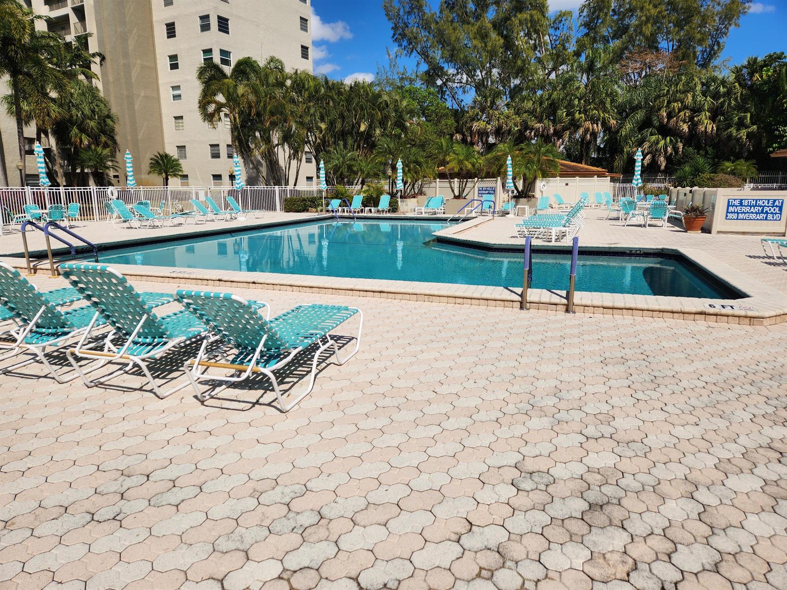 An outdoor swimming pool area with lounge chairs, umbrellas, and a multi-story building — 3940 Inverrary Boulevard # 302, Lauderhill FL 33319, LAUDERHILL, FL
