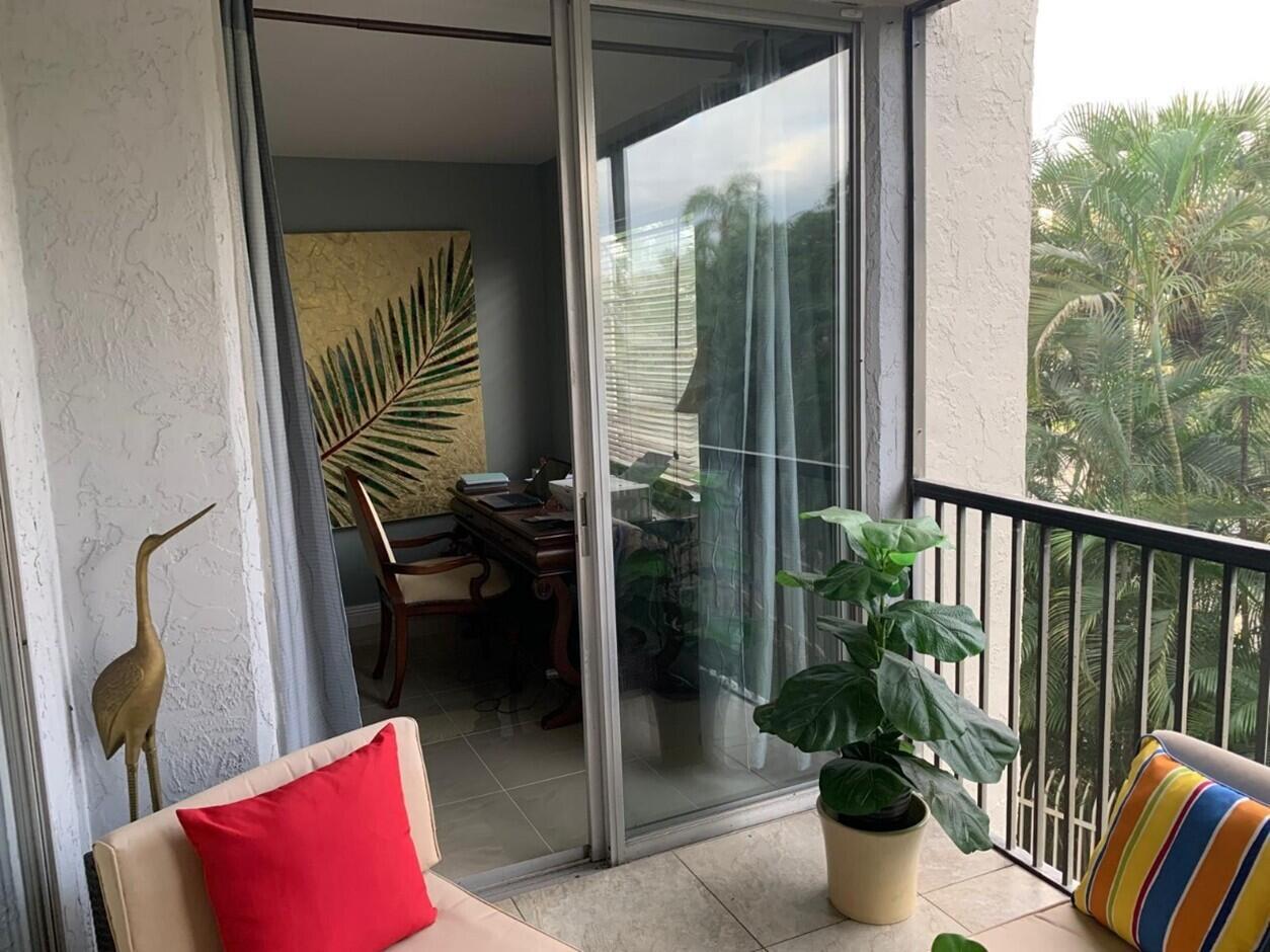 A balcony with a red pillow and potted plant overlooks a home office through glass doors — 3940 Inverrary Boulevard # 302, Lauderhill FL 33319, LAUDERHILL, FL