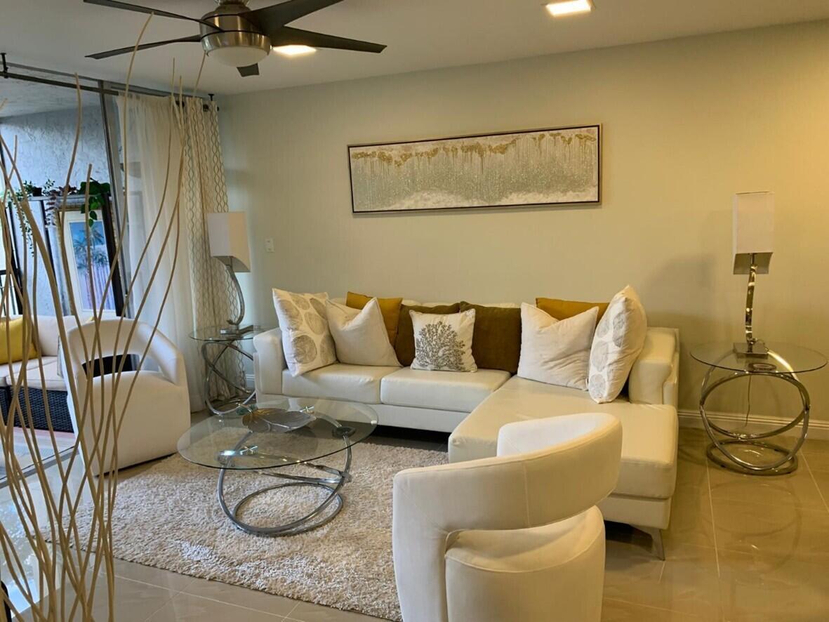 A living room features a white sectional sofa, glass coffee table, and two white armchairs — 3940 Inverrary Boulevard # 302, Lauderhill FL 33319, LAUDERHILL, FL