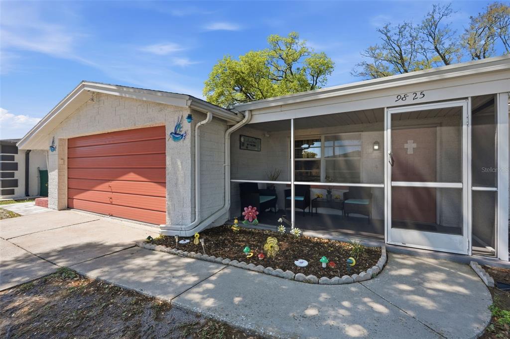 A single-story house features a red garage door, a screened-in front porch, and a landscaped garden — 9825 LAKESIDE LANE, PORT RICHEY, FL